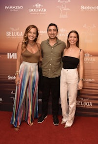 three people standing on a red carpet at an event