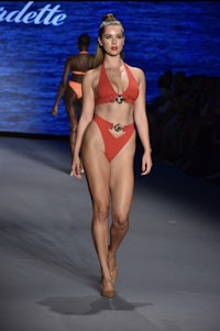 a model walks down the runway in an orange bikini