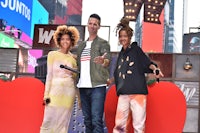 three people posing in front of a heart sign in times square