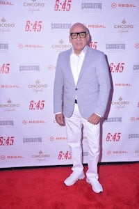 a man in a white suit standing on a red carpet